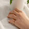 Hand wearing 14K yellow gold birthstone stackable rings with 2mm round stones sizes 4-10 on a white fabric with green plant in background  
